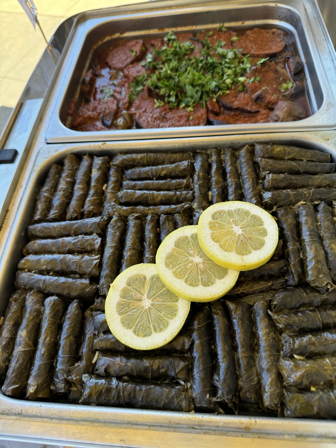 Tray of stuffed grape leaves with lemon alongside another catered dish